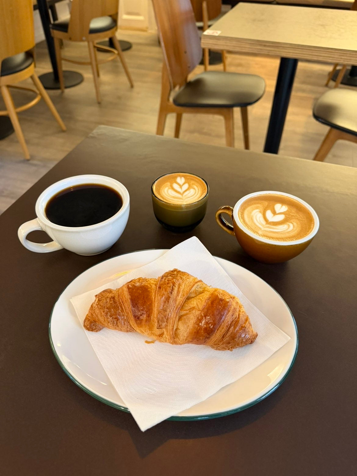 Croissant på tallerken med sort kaffe, cortado og latte i Bills Coffee